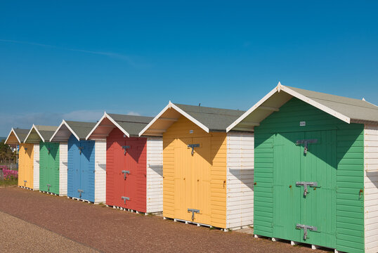 Brightly coloured beach huts with diminishing perspective  against a clear blue sky.