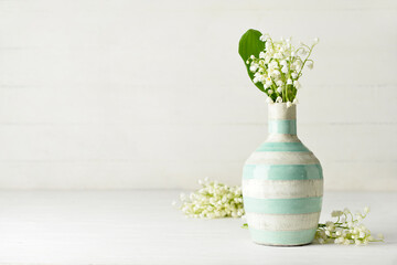 Vase with beautiful lily-of-the-valley flowers on light wooden background