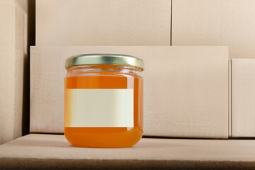 Photo of honey jar product with blank label standing on stacked cardboard boxes background.