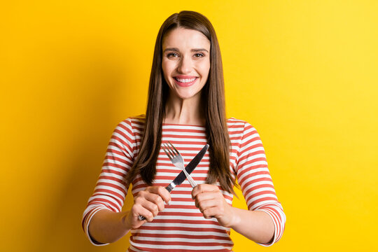 Portrait of attractive cheerful girl holding crossed cutlery waiting meal isolated over bright yellow color background