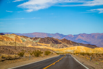 Fototapeta na wymiar Two land black topped road through Death Valley California USA with multi-covered hills ahead - Geological rift valley and lowest point in North America