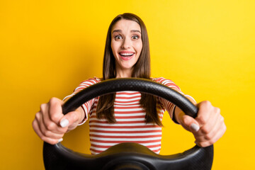 Portrait of attractive cheerful girl holding steering wheel driving race having fun isolated over bright yellow color background