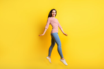 Fototapeta na wymiar Full length body size profile side view of pretty cheerful girl jumping walking isolated over bright yellow color background