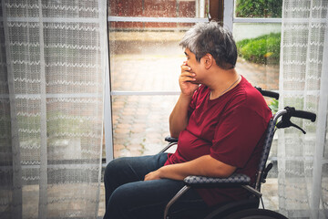 Asian fat man is upset and stressed, He was a patient sitting in a wheelchair, while the rain falling with alone, to people diabetes and health care concept.