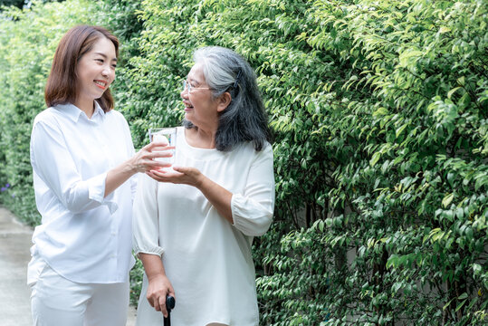 Portrait images of Asian woman nursing care handing a glass of water to elderly woman, with green nature background, to nursing care home and elderly health care concept.