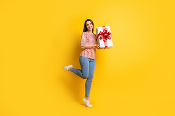 Full length body size view of attractive cheerful girl jumping holding gift having fun isolated over bright yellow color background