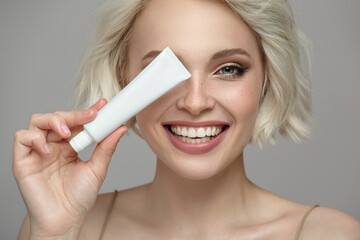 Portrait of a joyful girl with a snow-white smile holding a tube of toothpaste in her hand - 441013610