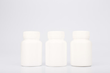 Three white plastic medication bottles in a row isolated on white background. Concept of medical treatment and prescription drugs