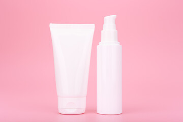 Close up of two white cosmetic bottles with cream, lotion, balm or scrub for face or hands on pink background. Concept of daily beauty routine for glowing, young looking skin 