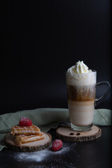 A freshly baked waffle with raspberries and powdered sugar and coffee latte macchiato served on the wooden plates