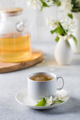 A mug of green tea with jasmine on the background of a teapot of tea and a branch of jasmine.
