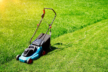 Lawnmower on a lush green lawn, half of the grass trimmed. Back yard of the house.