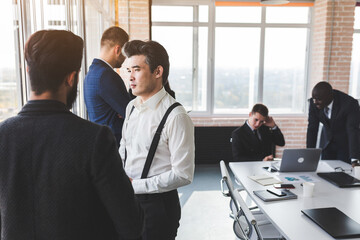 Mature businessman to discuss information with a younger colleague. People working and communicating while sitting at the office desk together with colleagues sitting.