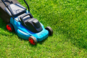 Lawnmower on a lush green lawn, half of the grass trimmed. Back yard of the house.