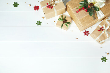 Border of gift boxes wrapped in kraft paper decorated with red berries, white ribbons and Christmas greenery on white wood desk background Xmas, winter, holiday concept. Flat lay, top view, copy space