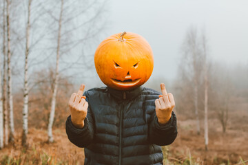 a man with a Halloween pumpkin on his head in a foggy field shows a fuck