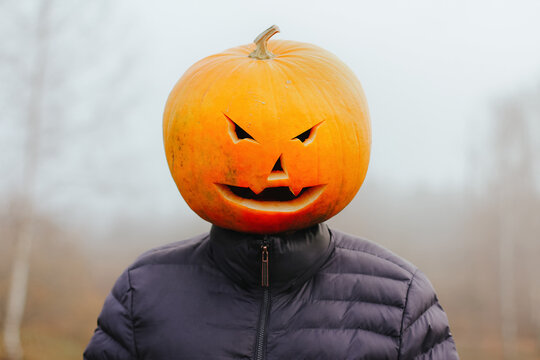 a man with a Halloween pumpkin on his head in a foggy field