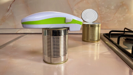 Electric can opener and canned goods on kitchen table - obrazy, fototapety, plakaty