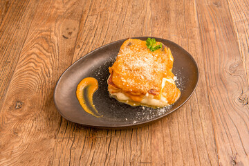Typical Italian recipe for pumpkin lasagna, provolone cheese and grated cheese on a black plate