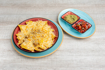 Corn nachos au gratin with grated cheese and beans and two separate bowls of guacamole and pico de gallo