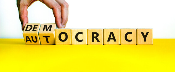 Democracy or autocracy symbol. Businessman turns wooden cubes and changes the word autocracy to...