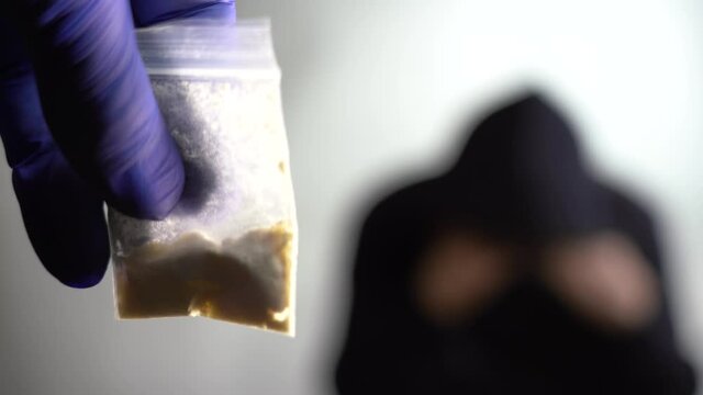 The concept of combating drug trafficking. The drug dealer is caught red-handed. A hand in a lilac medical glove holds a packet of drugs in the foreground, close-up.