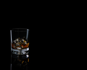 Glass of Kentucky Bourbon on rocks on black background with reflection on dark surface and space for copy text on the right side