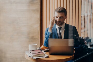 Portrait of elegant finance man in stylish suit sitting in cafe with open laptop