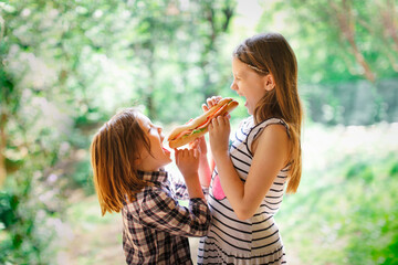 Take a bite. Funny cute Caucasian children are eating together a big sandwich. Concept food on the go, snack, food and siblings. Children share food with each other, sister treats to sandwich