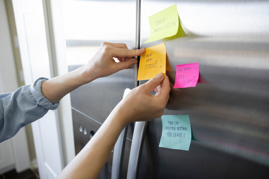 Woman Placing Adhesive Note Reminders On Stainless Steel Fridge Door