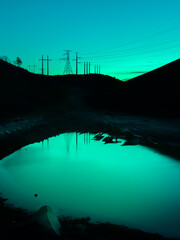 Industrial Turquoise Background Landscape with Electricity Pylons on the Hills. Twilight Silhouettes of Electric Poles and Cables. Water Reflections with Space for Text or Design