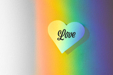 Light refracted on the wall forming a rainbow with a paper heart on it. Background with gay...