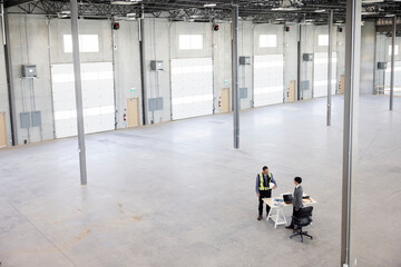 Contractor and architect working on desk in empty warehouse