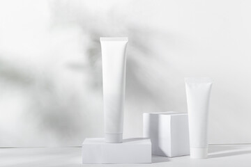 A set of white cosmetic jars on square stands with shadows. Toothpaste, face and body cream, hair shampoo. Professional cosmetics for skin care. Organic cosmetics.