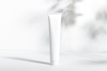 White cosmetic tube on a white background with leaf shadows. Nourishing and moisturizing face cream, hand cream or lotion. Women's cosmetic tube with a skin care product. Organic cosmetics, copy space
