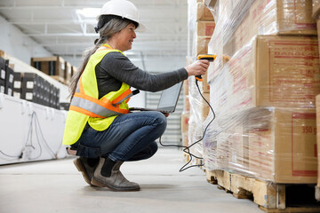 Female warehouse worker scanning pallet of cardboard boxes