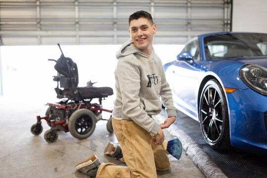 Portrait smiling disabled male worker detailing blue sports car