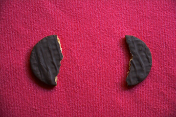 Two chocolate coated cookie halves separated with space in between on pink background with copy space.