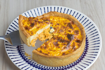 slice of chicken-flavored quiche lorraine with cream cheese being cut, wooden base
