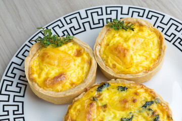 three roasted lorraine quiches on a patterned plate, wooden base