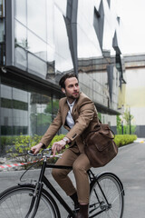 Fototapeta na wymiar full length of young businessman in earphones riding bicycle near building.