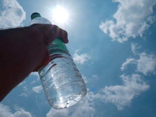 Mineral water bottle holding on hand towards sun light on sky, dehydration concept.