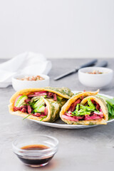 Egg rolls filled with pastrami, vegetables and green onions on a plate, sprouted grains and soy sauce in bowls on the table. Hearty and high-calorie snack. Vertical view. Copy space