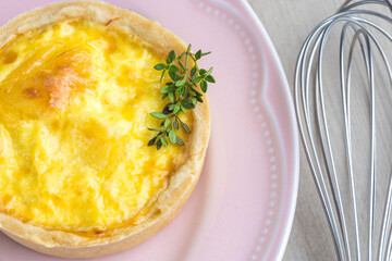 Lorraine cheese quiches with thyme detail on a pink plate, fuet on the side on a wooden base