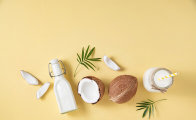 Fototapeta na wymiar Healthy flat lay concept. Vegan milk bottles, coconut slices and palm branch on yellow background. Top view and copy space