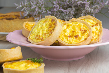 cheese lorraine quiches on a pink plate, some cheese and mint decorative elements, wooden base