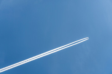 Flying airoplane on the blue sky leaving white lines behind