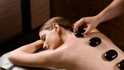 Masseur placed hot stone on the back of woman. Manual therapy in spa.