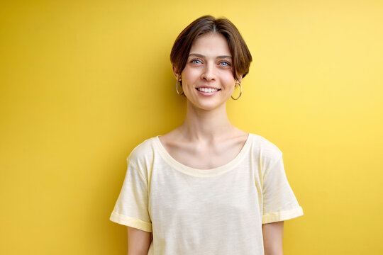 Portrait of adult woman cutely smiling posing at camera, isolated over yellow background, dressed casually. dreamy adorable woman with short hair