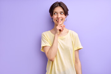 Young caucasian woman over isolated purple background doing silence gesture, has secret, looking at side, dressed casually. portrait of female with short brown hair